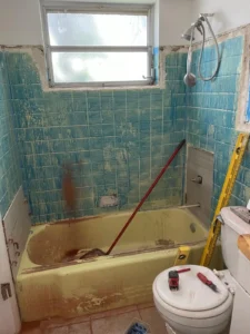 Outdated bathroom before renovation with old turquoise tile and yellow tub in Miami home.